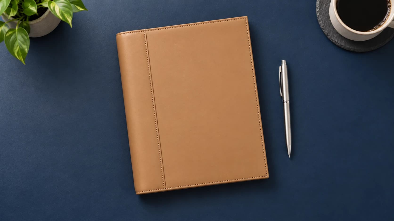 Closed tan FranklinPlanner Noah leather binder and silver pen on a navy surface
